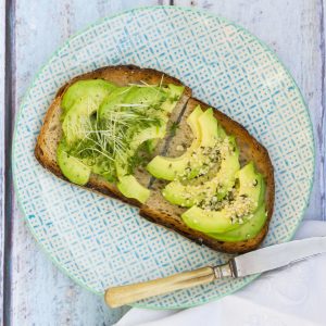 Slice of toasted bread with acocado, cress and hemp seeds on a plate