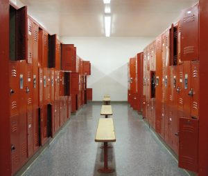 Interior of gym locker room with benches and lockers, some open and some closed.